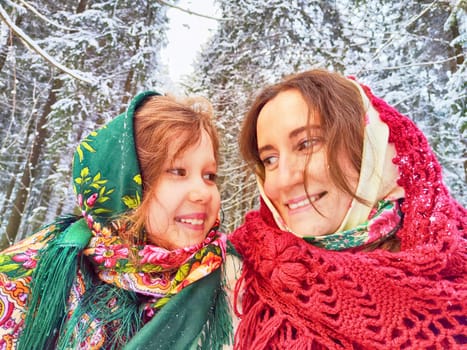 Portrait of happy family. Mother and daughter in shawls in winter forest. Ethnic clothes for carnival Maslenitsa