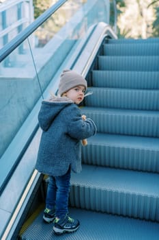 Little girl with a soft toy rides up an escalator looking back. High quality photo