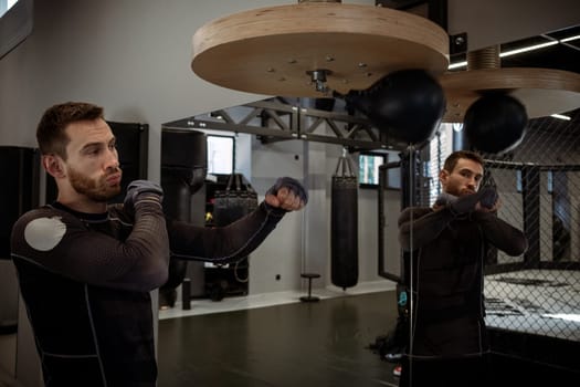 Concentrated young adult bearded boxer honing skills on speed bag, working out focus and accuracy in well-equipped boxing gym