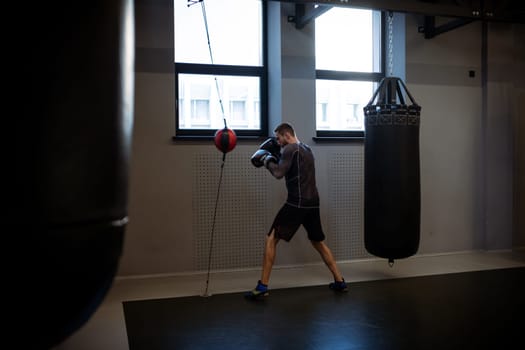 Determined adult man in sportswear and boxing gloves training with floor to ceiling bag, strengthening muscles, improving reflexes and punching speed in gym setting