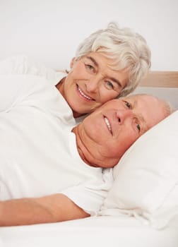 Senior couple, portrait and together in bed, relaxing and love in retirement for bonding on weekend. Elderly people, bedroom and resting or happy in marriage, romance and morning routine at home.