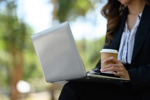 Businesswoman using laptop, working online in the city park on beautiful day.