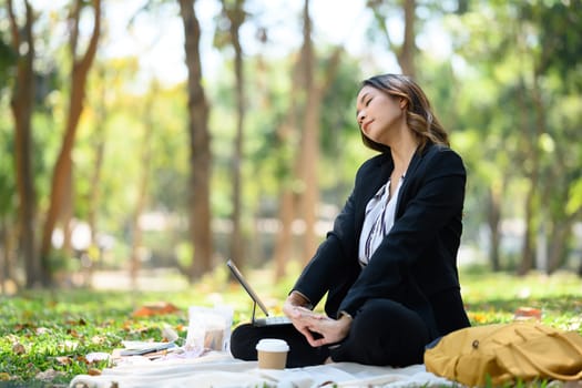 Calm businesswoman relaxing in the park against sunlight. Urban lifestyle concept.