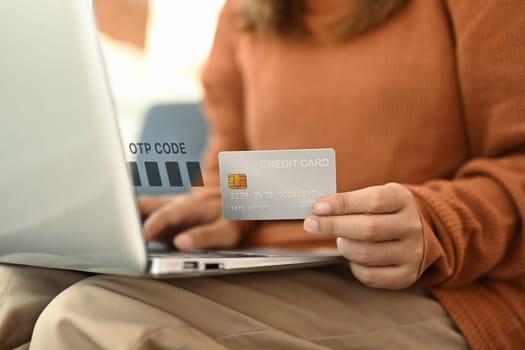 Young woman holding credit card and entering verification code login to bank account on laptop.