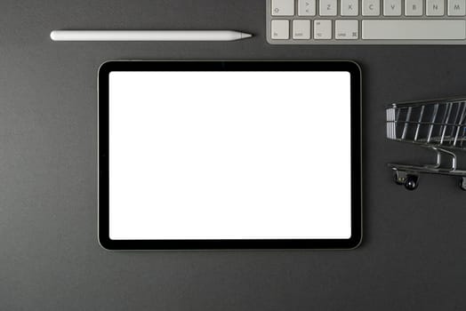 Tablet with blank screen, keyboard and supermarket cart on dark gray office desk