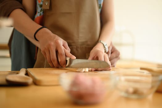 Woman in apron chopping garlic on wooden board, couple preparing food meal in the kitchen.