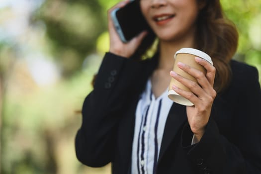 Businesswoman executive holding paper cup of coffee and talking on mobile phone at outdoor.