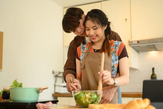 Loving young couple embracing and making healthy salad in the kitchen. Healthy lifestyle concept.