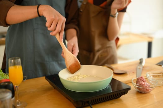 Man wearing apron sauteing garlic in the frying pan, cooking with his wife in the kitchen.