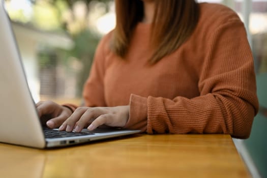 Female freelancer working on a laptop computer, typing message or chatting online with client.