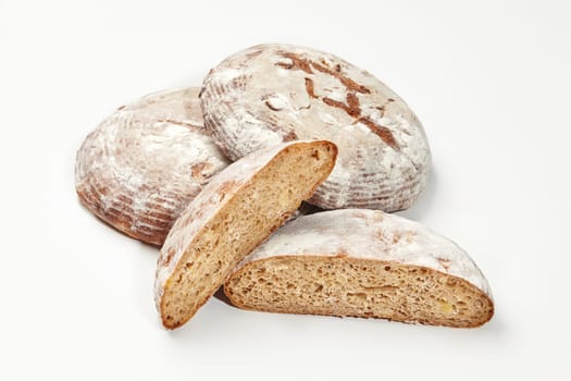 Three artisan wheat bread loaves with one cut in half, isolated on white background, showcasing crust and airy texture. Traditional bakery products concept