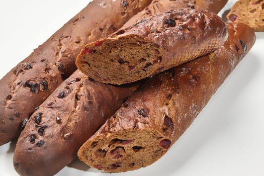 Artisanal cranberry studded rye baguette, whole and sliced against white backdrop with focus on grainy texture and crimson dried berries. Breadmaking concept