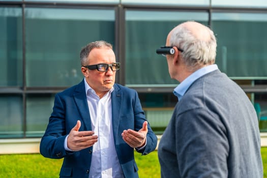 Aged businessmen coworkers using an augmented reality device while talking outdoors