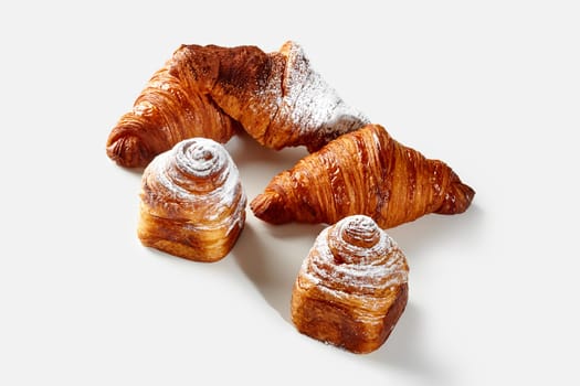 Delightful golden flaky classic croissants and cube shaped cruffins, dusted with powdered sugar and cocoa, arranged on white background. Sweet French style pastries