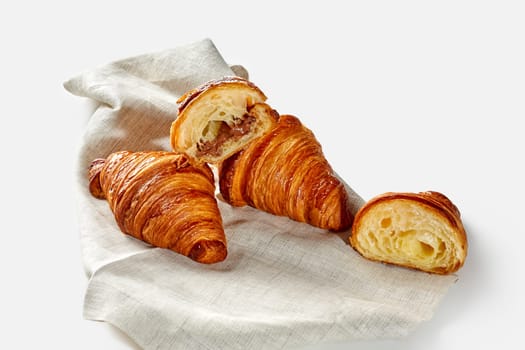 Flaky and delicately sweet croissants with nut and chocolate filling arranged on linen cloth, isolate on white background. Modern confectionery in classic French tradition