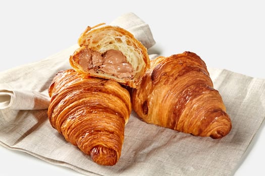 Gourmet fluffy croissants with rich chocolate cream filling, resting on natural linen napkin, exuding warmth and bakery freshness. French style viennoiserie pastry