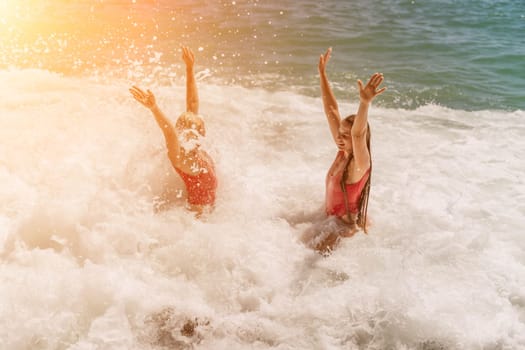 Women ocean play. Seaside, beach daytime, enjoying beach fun. Two women in red swimsuits enjoying themselves in the ocean waves and raising their hands up