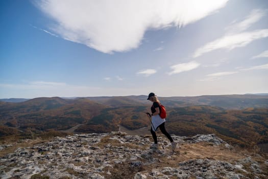 woman on mountain peak looking in beautiful mountain valley in autumn. Landscape with sporty young woman, blu sky in fall. Hiking. Nature.