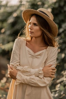 Woman with straw hat stands in front of vineyard. She is wearing a light dress and posing for a photo. Travel concept to different countries.