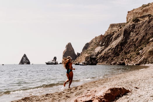 Woman beach vacation photo. A happy tourist in a blue bikini enjoying the scenic view of the sea and volcanic mountains while taking pictures to capture the memories of her travel adventure