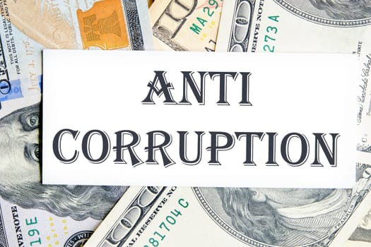 ANTI CORRUPTION text writing on a white card against the background of banknotes