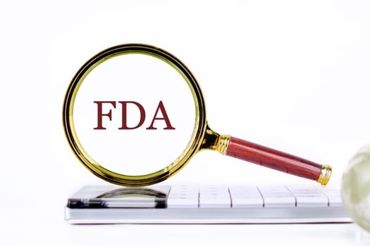Word FDA written through a magnifying glass on a calculator on a light background. Business development concept