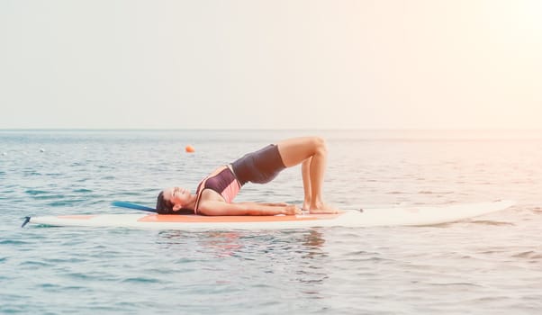 Woman sup yoga. Happy young sporty woman practising yoga pilates on paddle sup surfboard. Female stretching doing workout on sea water. Modern individual female outdoor summer sport activity