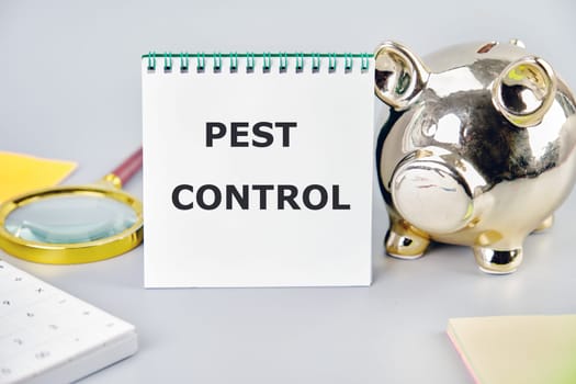 Pest control phrase written on a notebook on a gray background near a calculator, a piggy bank, and stickers. Small Business Concept