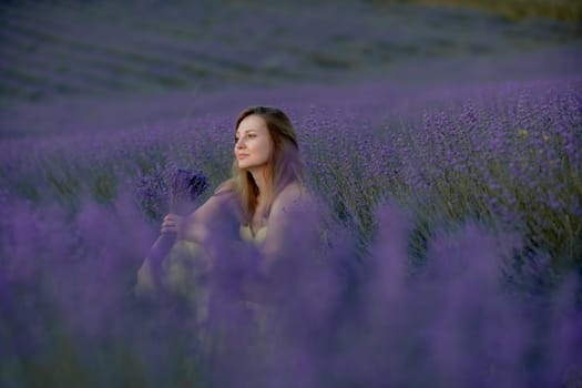 Woman poses in lavender field at sunset. Happy woman in yellow dress holds lavender bouquet. Aromatherapy concept, lavender oil, photo session in lavender.