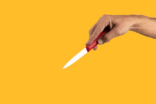 Black male hand holding a red cooking knife isolated on yellow background. High quality photo