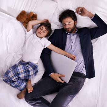 Tired, businessman and sleep with son, laptop for rest with technology and suit. Father, child and bedroom with fatigue, love and above with freelance peace or remote work for stress management.