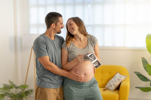 Pregnancy couple hugging looking picture of ultrasound, smiling happily touching belly. High quality photo