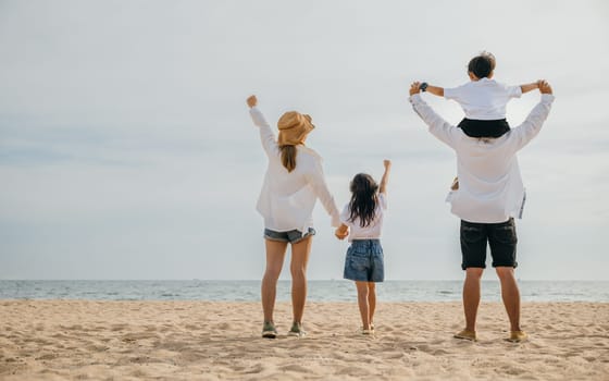 Sunset happiness at the sea beach, A family of four with raised arms. Father carries his son on shoulders creating a perfect portrait of carefree summer vacation enjoyment. Family on beach vacation