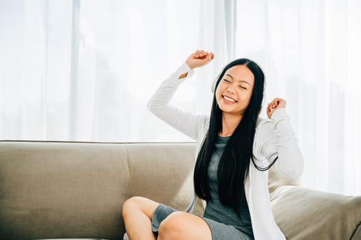 Enjoying her favorite music woman happily dances on the couch holding her smartphone with headphones on. Embracing the pleasure of music relaxation and entertainment at home. Vibrant leisure concept.