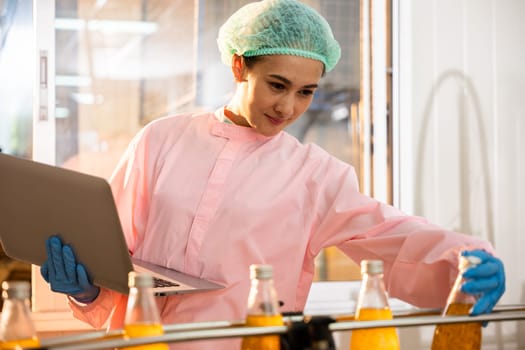 Quality manager a woman maintains liquid quality by inspecting beverage bottles on a conveyor belt. She utilizes a laptop for thorough quality control in the factory.