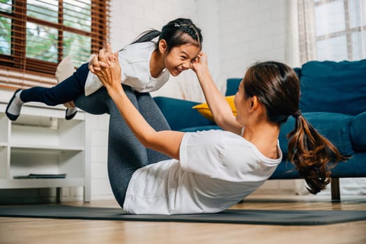 A little bird posture in family yoga as a mother holds her daughter on her feet creating a harmonious and joyful family moment at home. Laughter and smiles add to the fun.