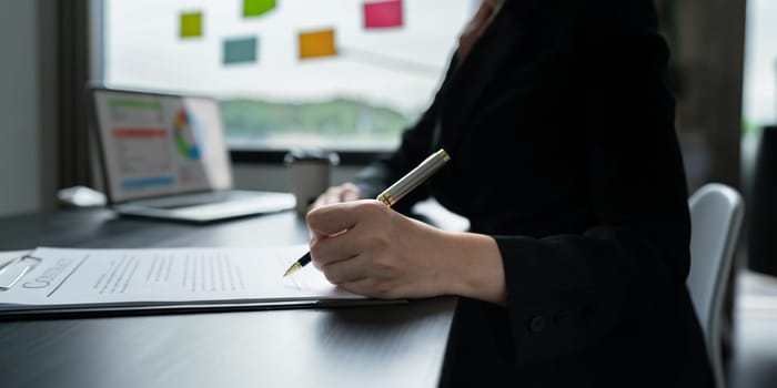 Close up image of businessman hand putting signature on contract document in presence of business partner.