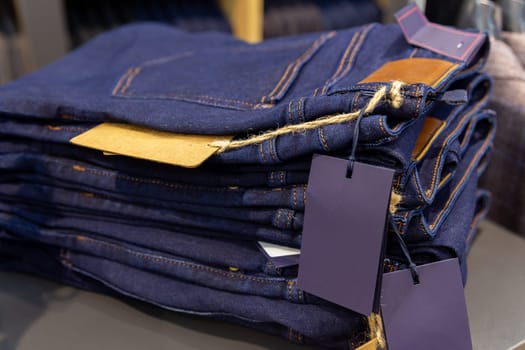 Close up denim jeans stacked in shop. Jeans a stack of folded pairs of blue pants on a shelf.