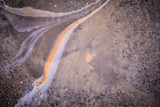 Beautiful spreading of oil or gasoline over the surface of water in a puddle on the asphalt.