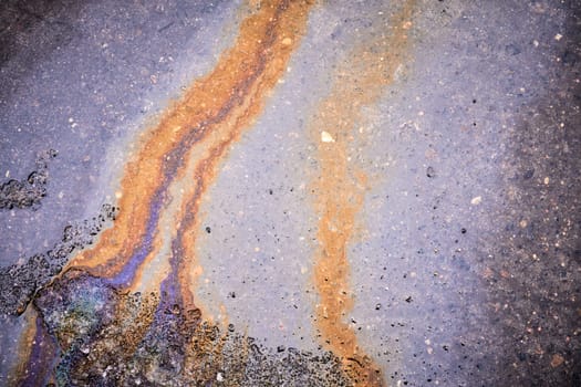 Textured stain of fuel or oil on wet asphalt on a rainy day.