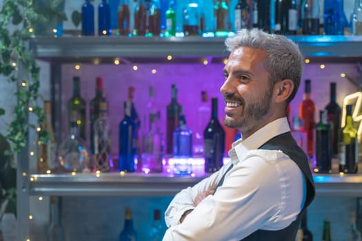 Barman portrait in a white shirt and black apron smiling at nightclub. High quality photo