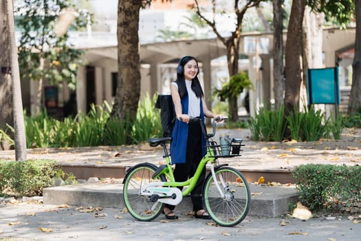 Asian young businesswoman bike to work for eco friendly green energy and listen music with headphone while commuting in city. Eco friendly.