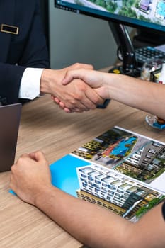 Two businessmen shaking hands over a blueprint plan in a modern office, symbolizing agreement in real estate development.