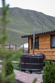 Wooden hot tub on the terrace of a house with a mountain landscape in the background. Relaxation and tranquility in nature.