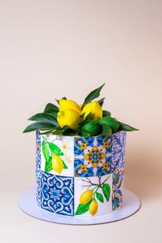 A round cake is decorated with lemons, green leaves, and ceramic tiles pattern. The cake is isolated on a beige background.