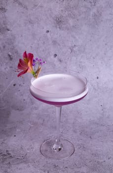 Elegant image of a pink cocktail in a glass with a flower garnish on a gray background, exuding class and sophistication.