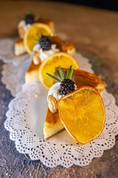 A decadent display of four slices of creamy cheesecake adorned with vibrant orange slices and juicy blackberries on a dainty white doily.