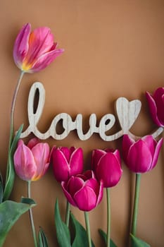 Wooden word LOVE message text. Beautiful pink tulip flowers around on beige neutral background. Concept of romance, valentines day celebration greeting card. Top view, flat lay. Template mock up