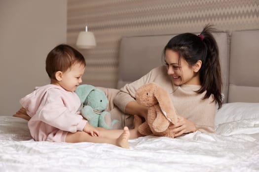 happy mother and her little child daughter playing with bunny toys in bedroom, family having fun