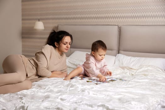 caucasian mother playing puzzle together with her little child girl in bedroom